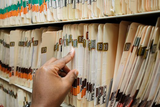 african american man sorting through stack of medical charts on shelves wearing a ring with black shirt