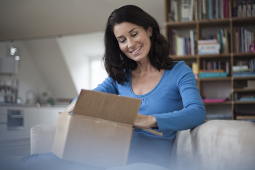 Smiling woman at home sitting on couch unpacking parcel